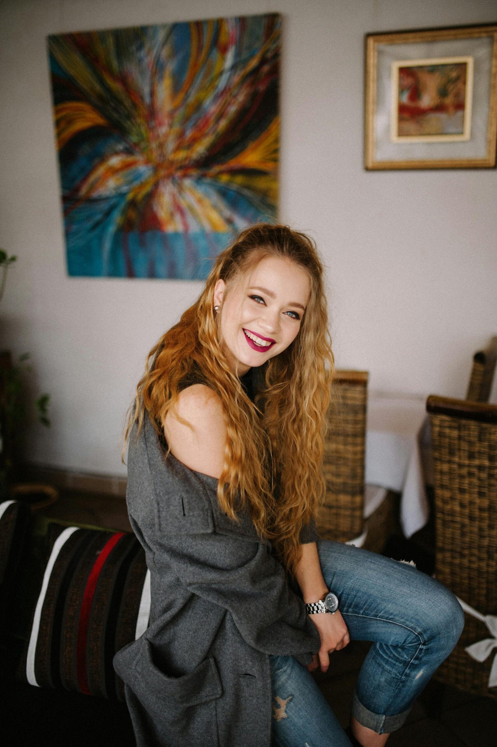 Cheerful young woman in a cozy home setting with vibrant abstract art on the wall.